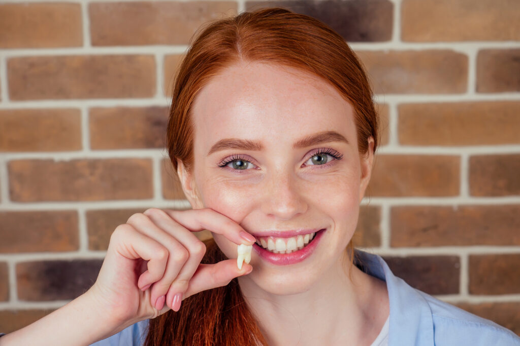 Jeune fille souriante tenant sa dent extraite dans la main.
